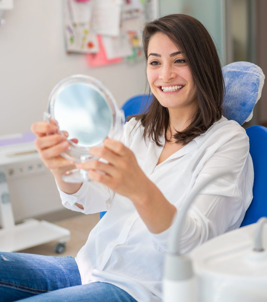 Stock image of a smiling female patient checking her teeth in mirror