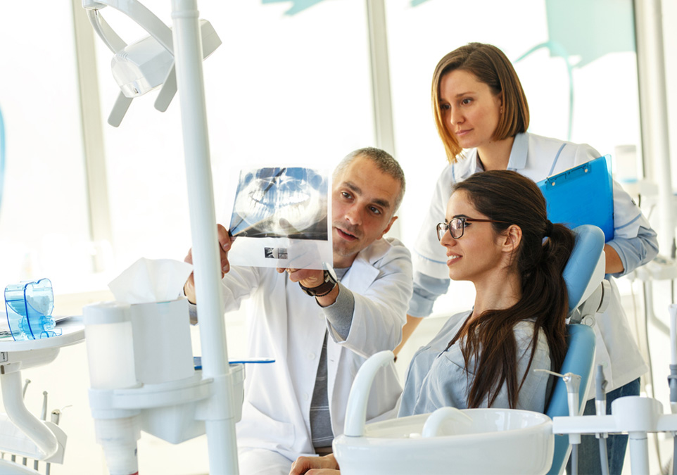 Stock image of a dentist showing dental xray to his patient along with dental assistant